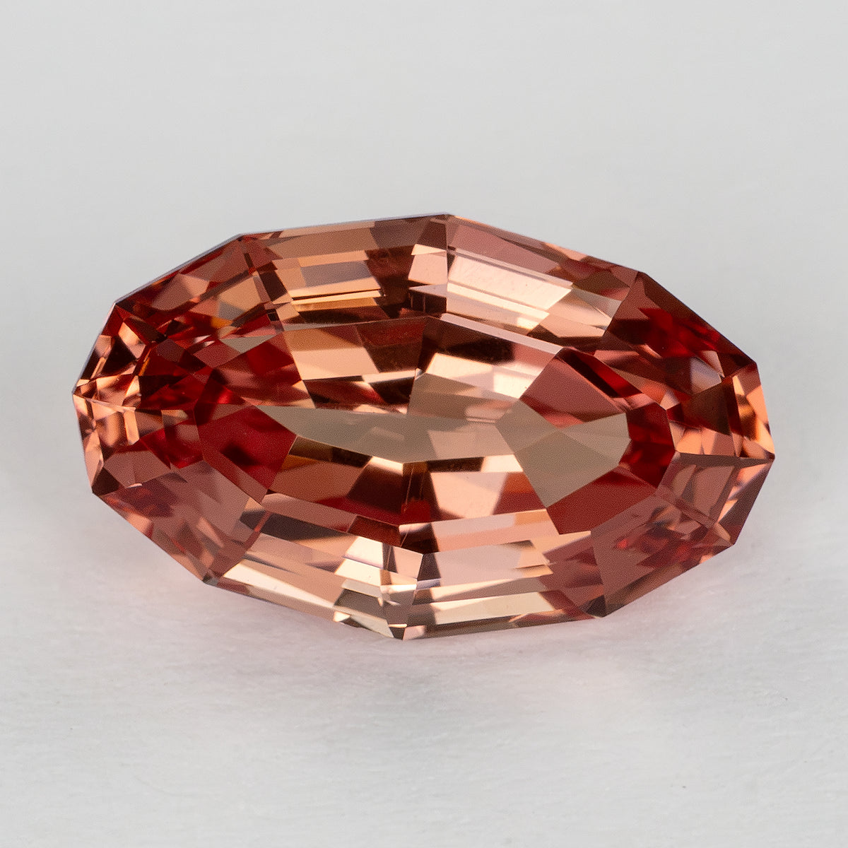 Close face-up view of the oval lab-grown sapphire with peach and orange-pink reflections across its step facets.