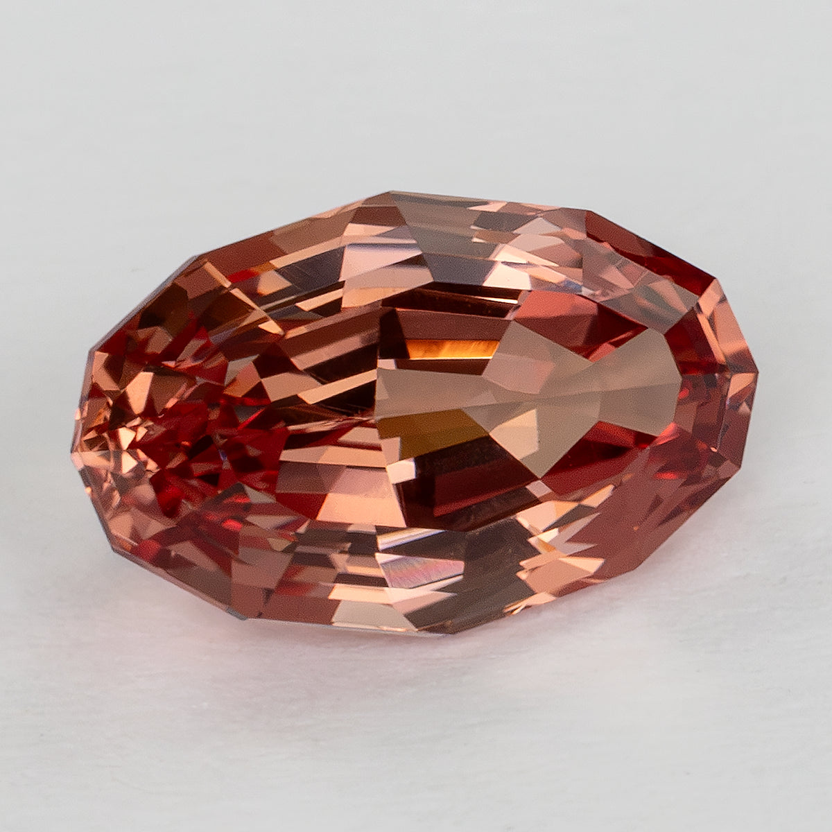 Angled face-up view showing the oval sapphire outline and warm orange-pink step-facet reflections.
