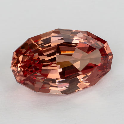 Angled face-up view showing the oval sapphire outline and warm orange-pink step-facet reflections.