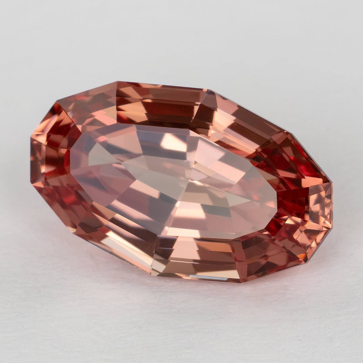 Oval lab-grown sapphire showing a lighter peach reflection across its broad central facets.