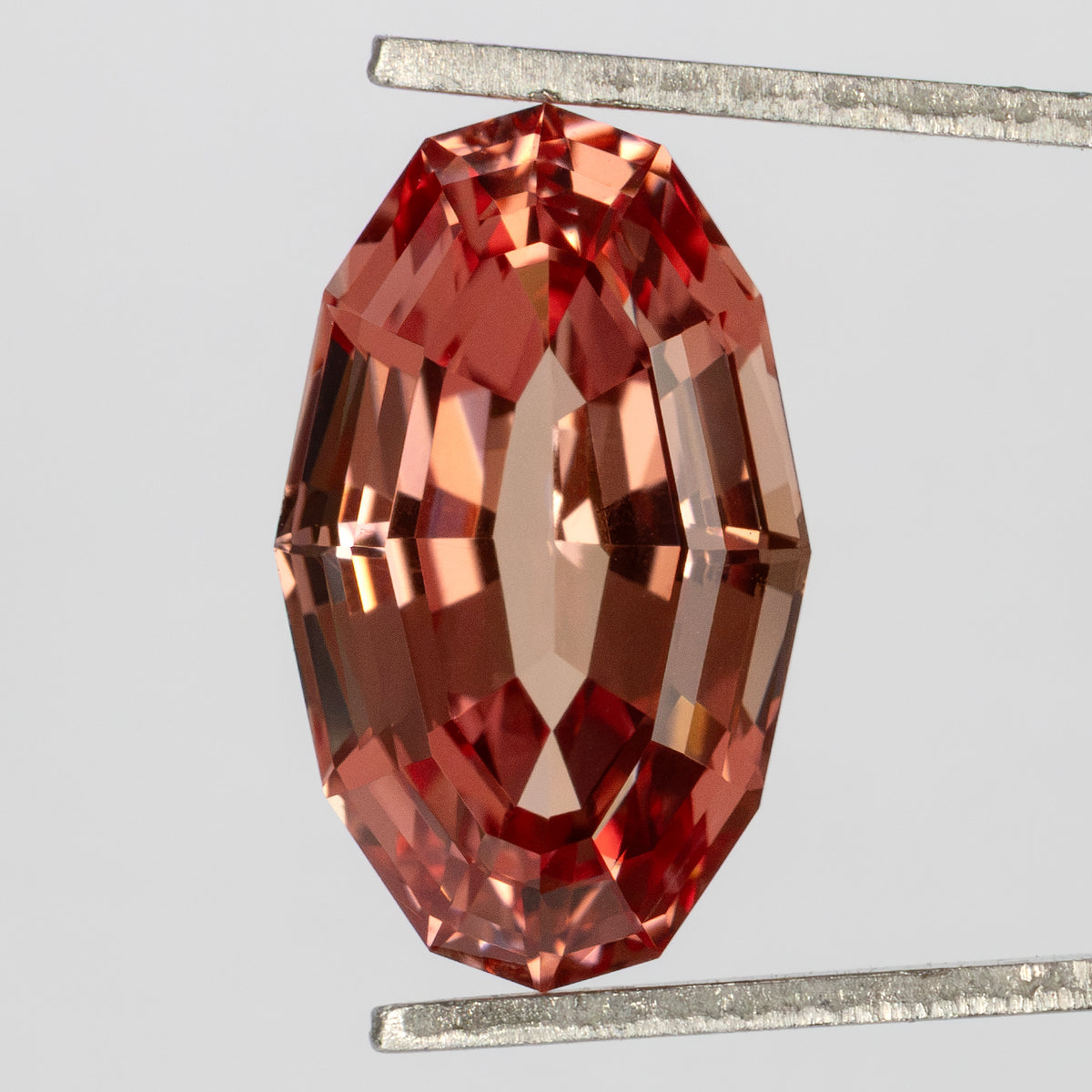 Upright tweezers-held view of the elongated oval sapphire and its broad facet pattern.