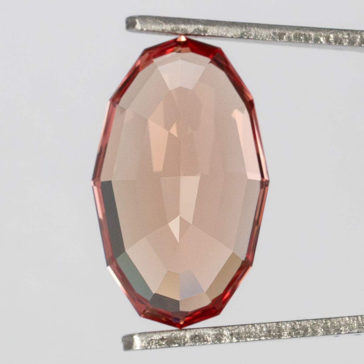 Back view of the oval sapphire held upright in tweezers, showing its pale peach pavilion.