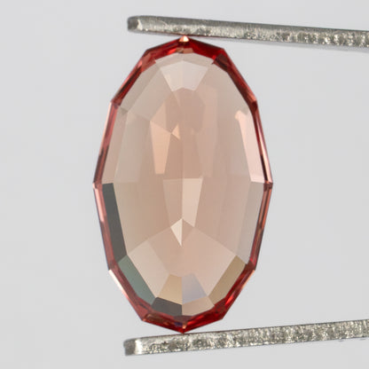 Back view of the oval sapphire held upright in tweezers, showing its pale peach pavilion.