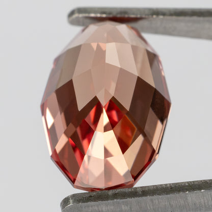 Tilted back view of the oval sapphire held in tweezers, showing the pavilion facets.