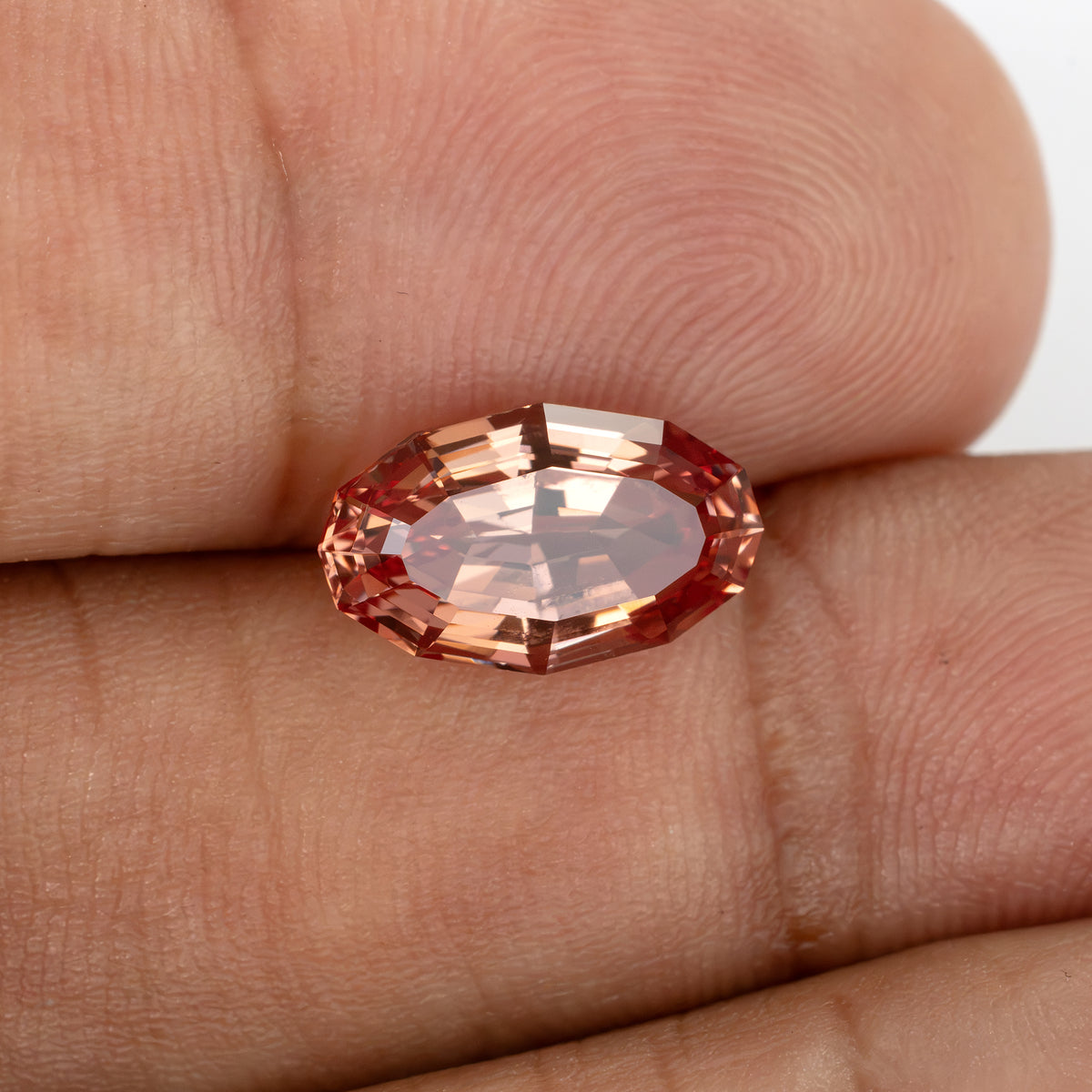 Oval orange-pink sapphire resting on fingers with pale peach reflections for scale and appearance.