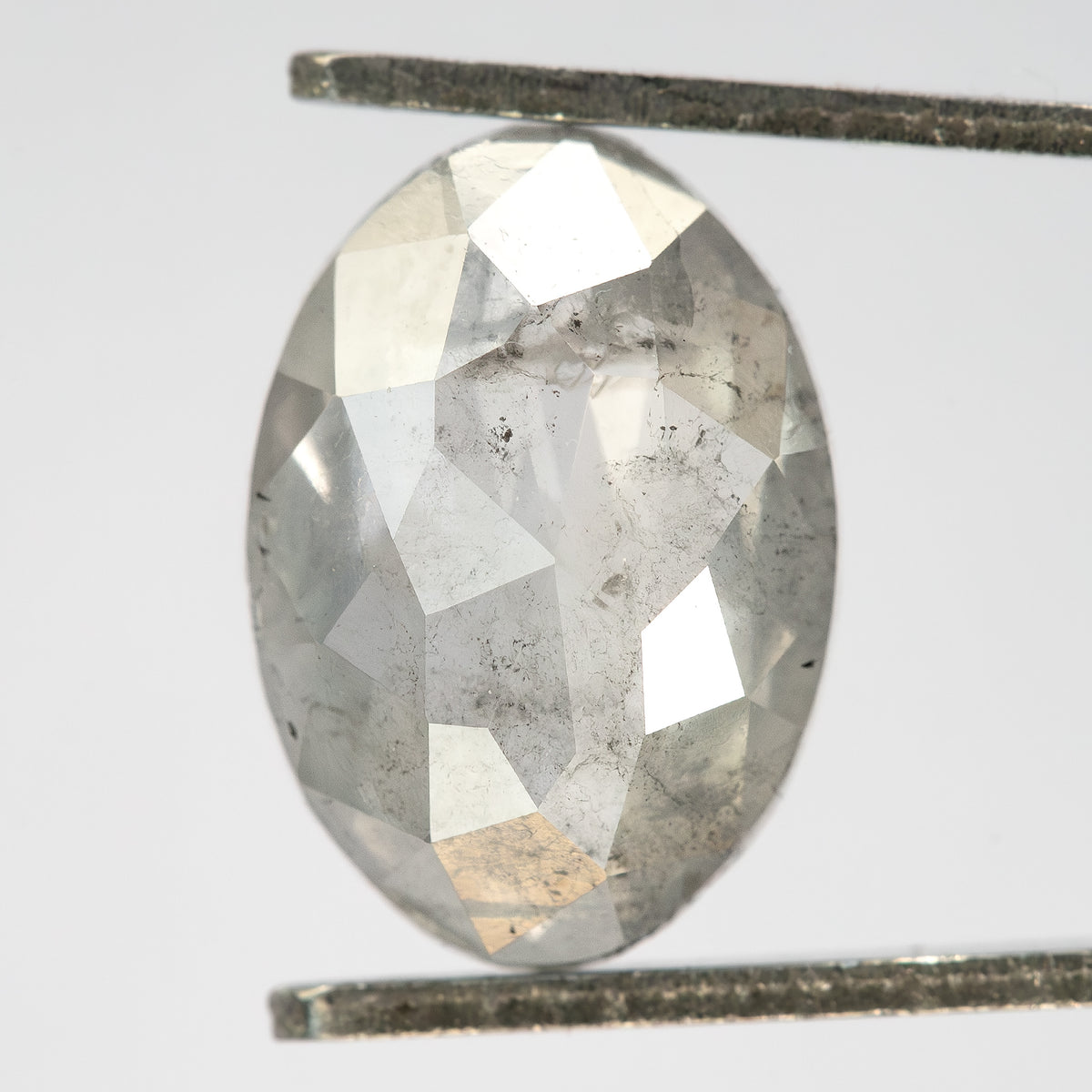 Oval pale gray diamond held upright in metal tweezers, showing broad rose-cut facets and visible inclusions.