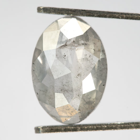 Oval pale gray diamond held upright in metal tweezers, showing broad rose-cut facets and visible inclusions.