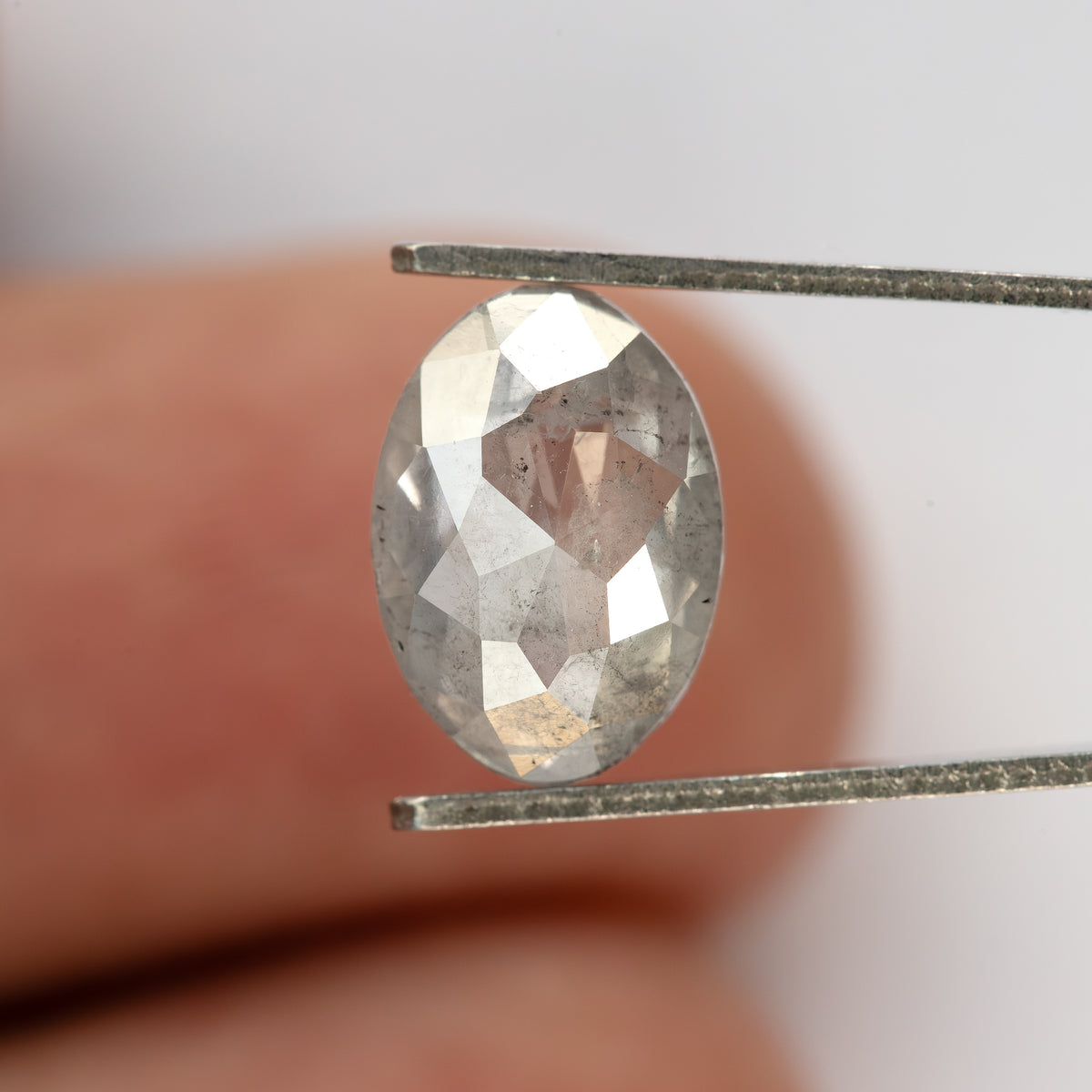 Oval diamond held in tweezers against a fingertip, showing its size and full outline.