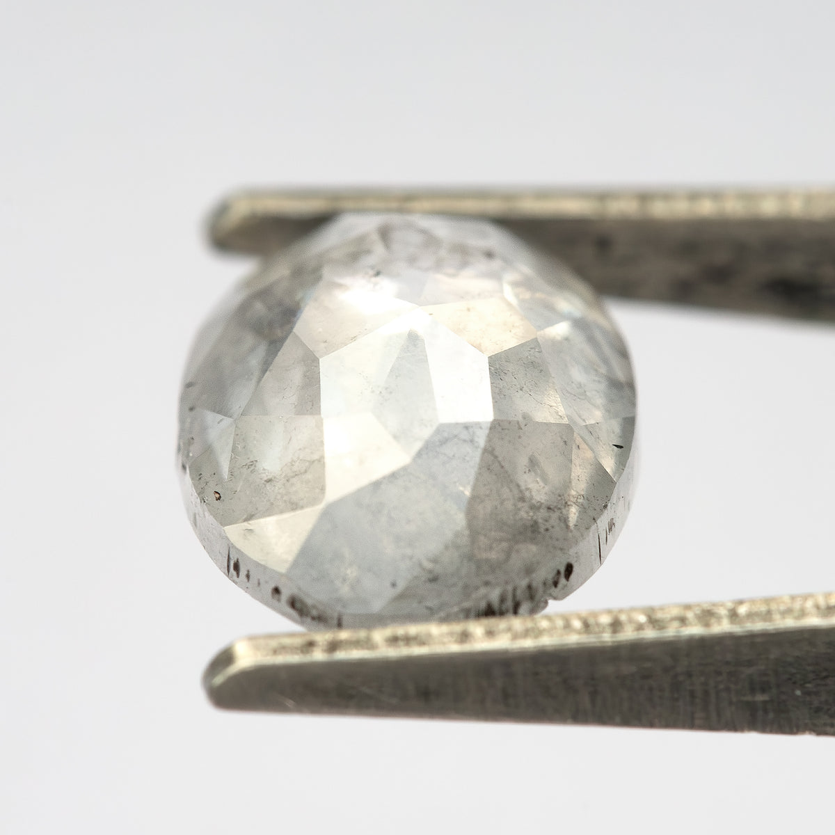 Oblique crown view of the oval diamond in tweezers, showing facet reflections and inclusions.