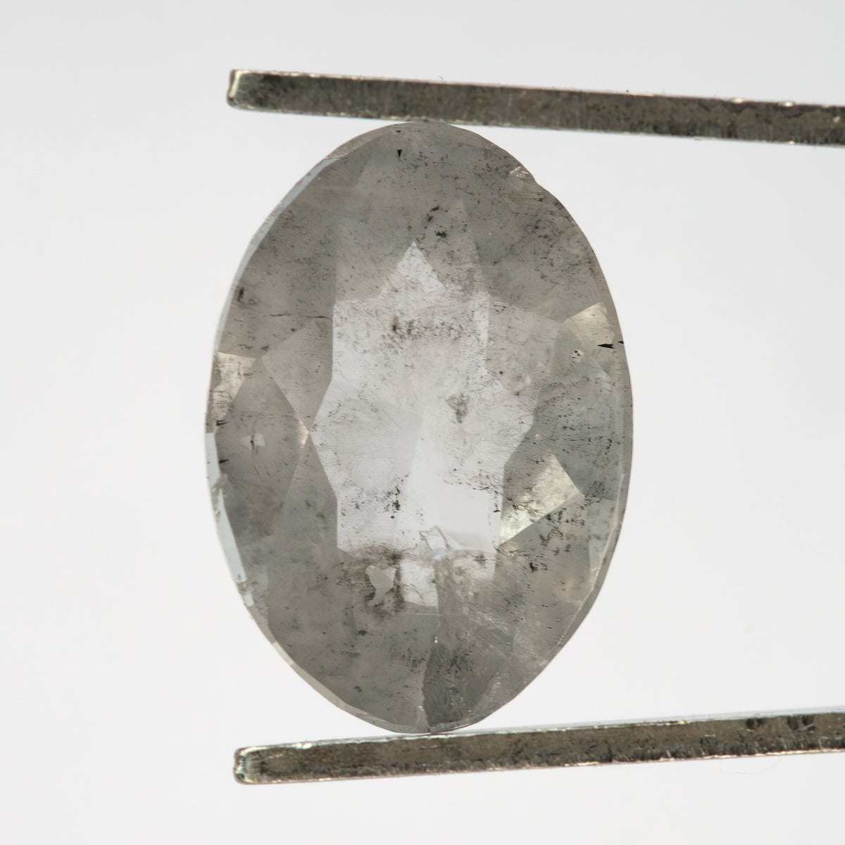 Reverse view of the oval diamond held upright in tweezers, with dark inclusions visible.