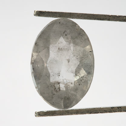 Reverse view of the oval diamond held upright in tweezers, with dark inclusions visible.
