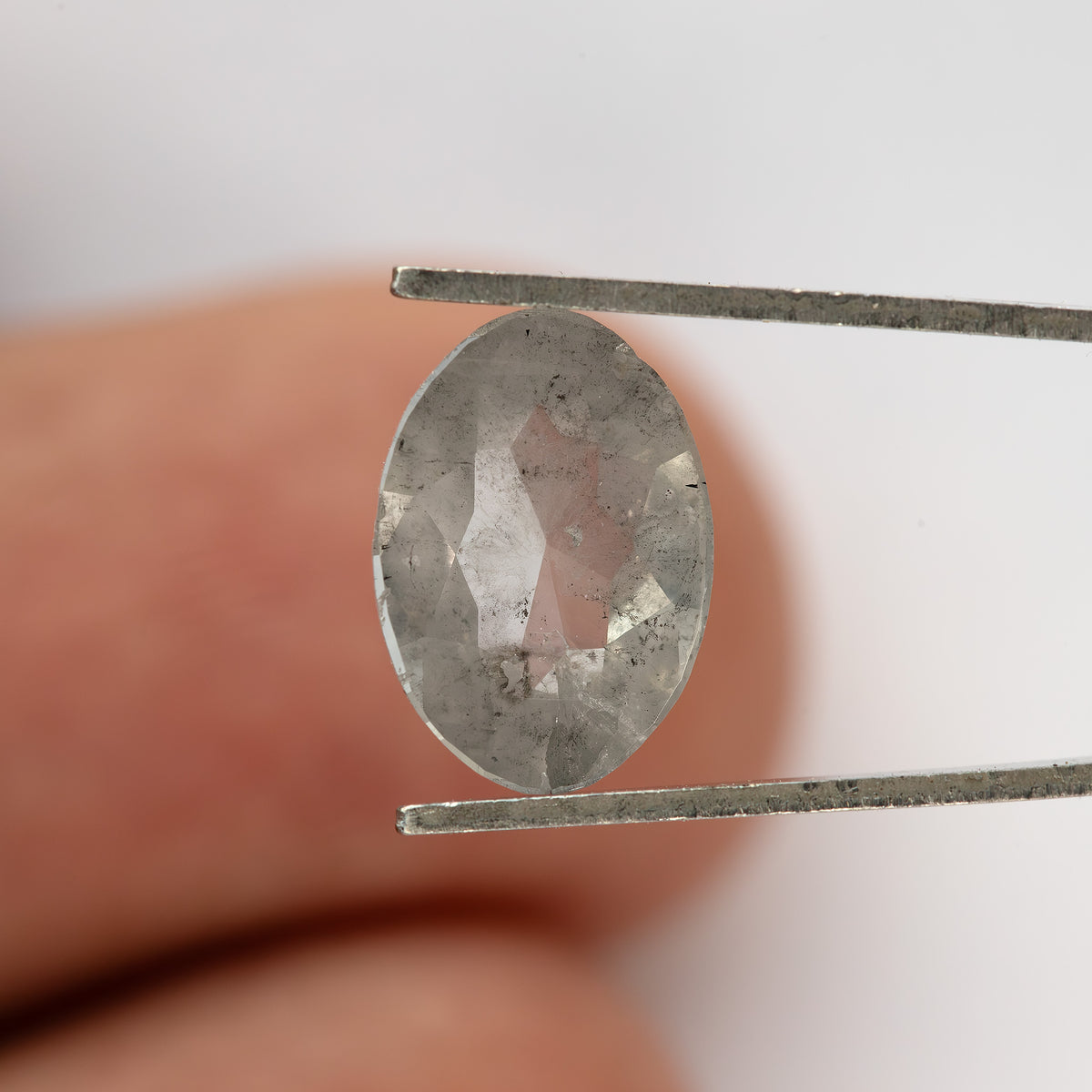 Oval diamond in tweezers against a fingertip, showing the reverse surface.