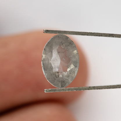 Oval diamond in tweezers against a fingertip, showing the reverse surface.