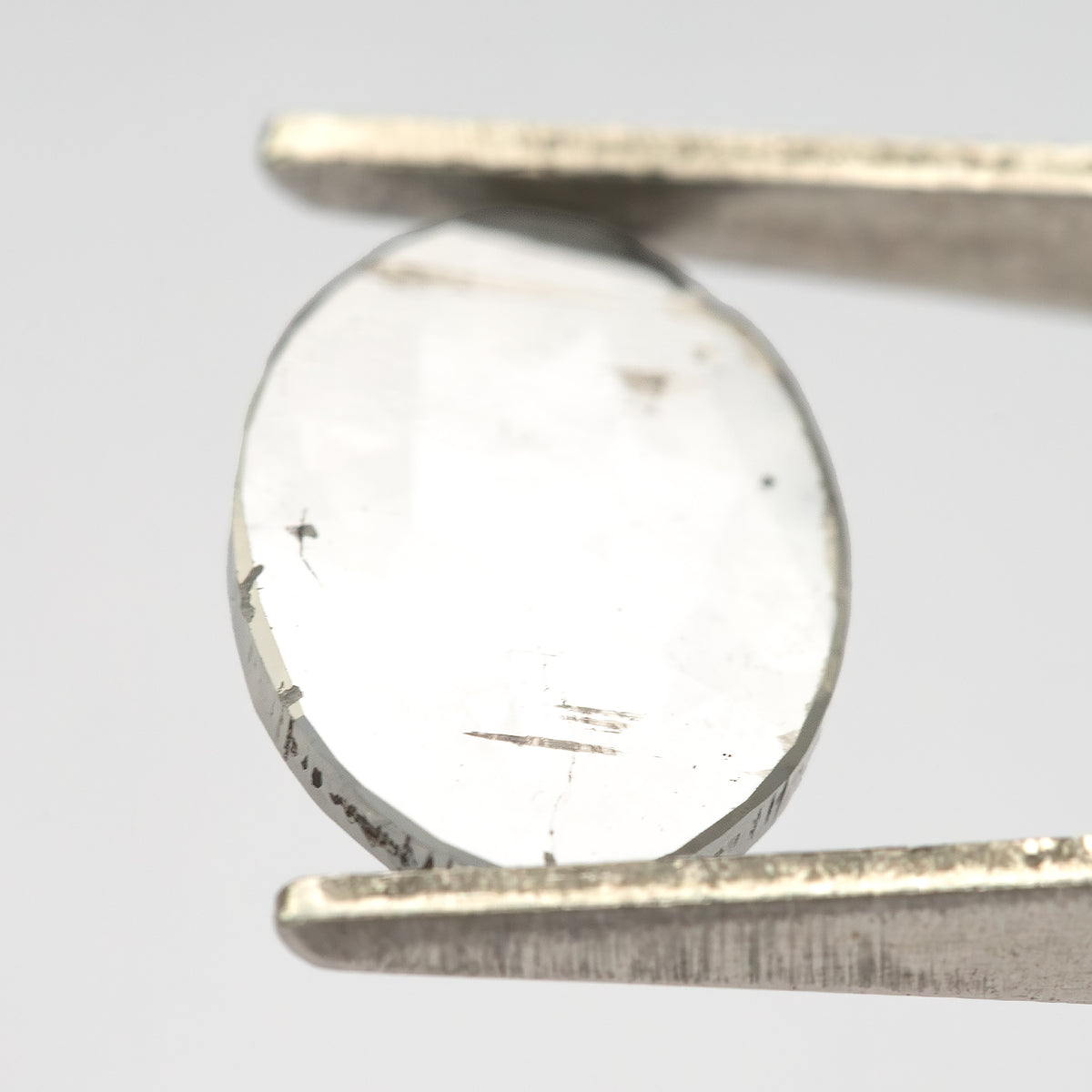 Oval diamond in tweezers at a bright reflective angle.