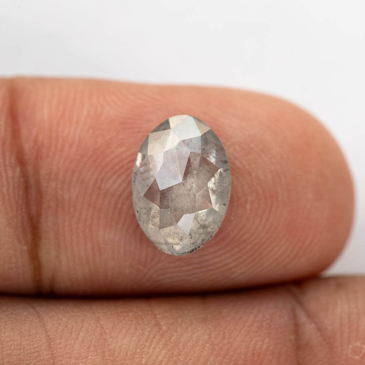 Oval diamond resting on a fingertip, with broad triangular crown facets.