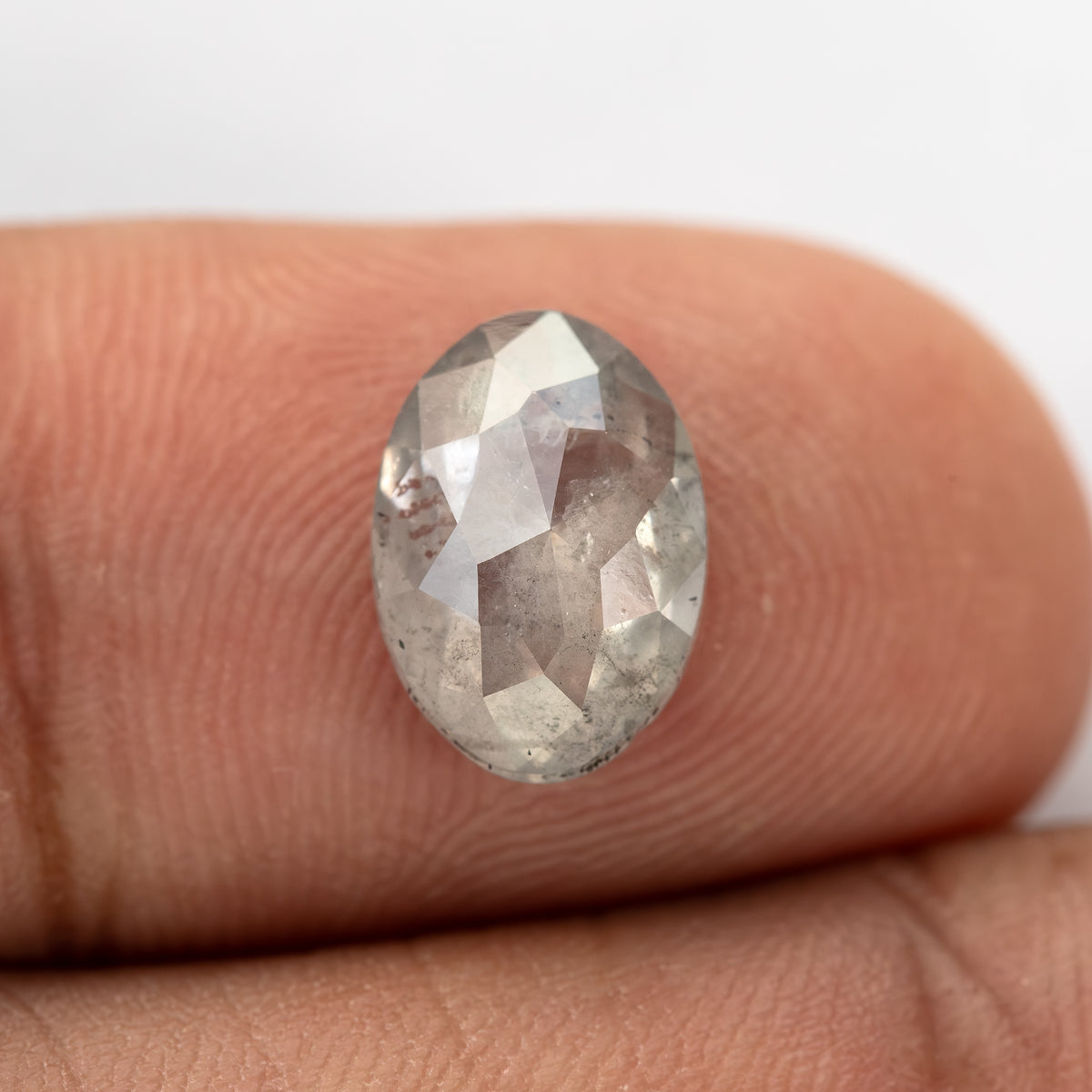 A second fingertip view of the oval diamond, showing its internal inclusion pattern.