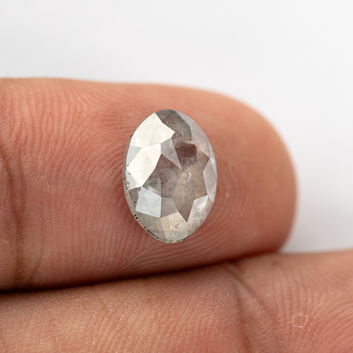 Oval diamond on a fingertip with shifting pale-gray facet reflections.
