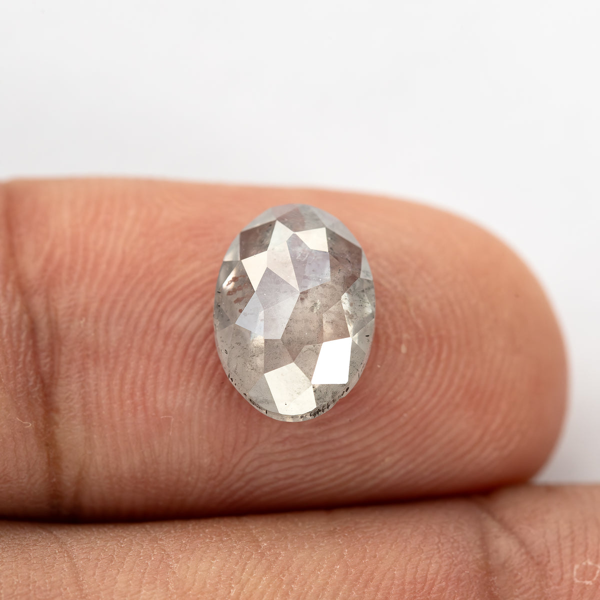 Closer fingertip view of the oval diamond, showing its full outline and inclusions.