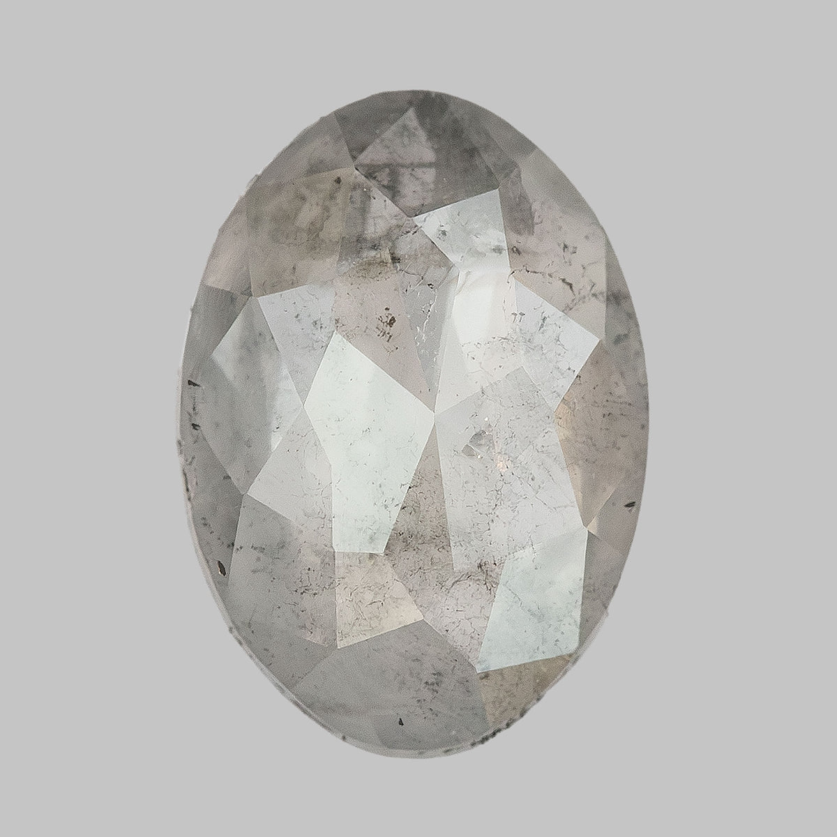 Oval diamond viewed upright on a pale surface, with visible dark inclusions.