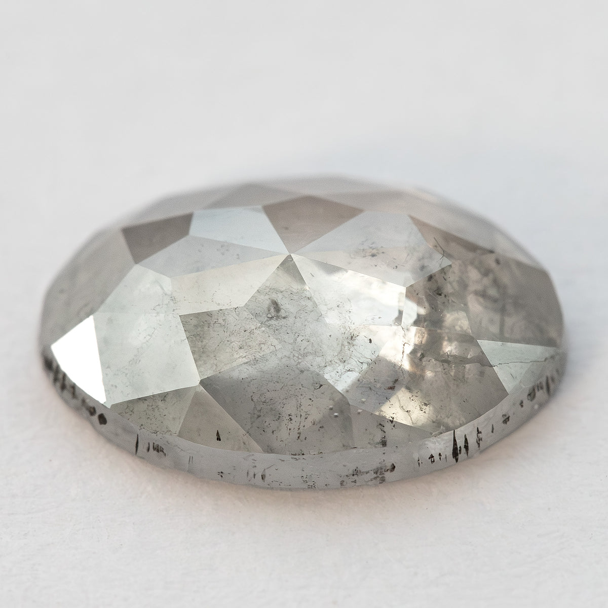 Low oblique view of the oval diamond on a pale surface, showing crown height.
