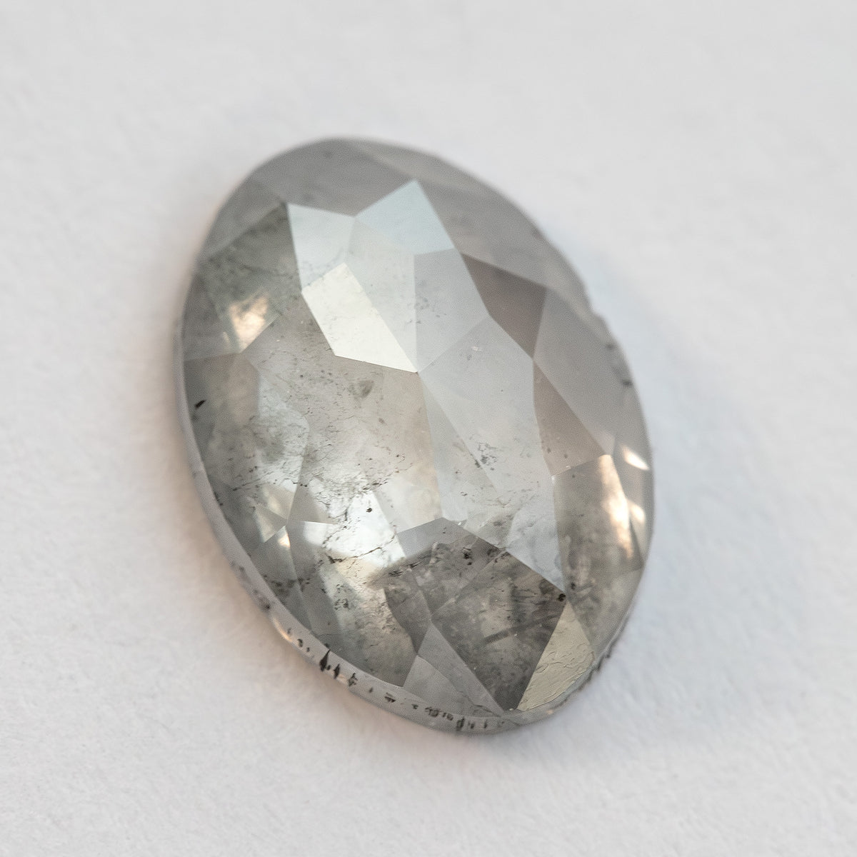 Oval diamond resting at a slight angle on a pale surface, with the crown and girdle visible.