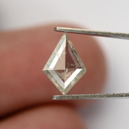 Kite diamond held in tweezers in front of a fingertip, showing the full outline and transparent areas.