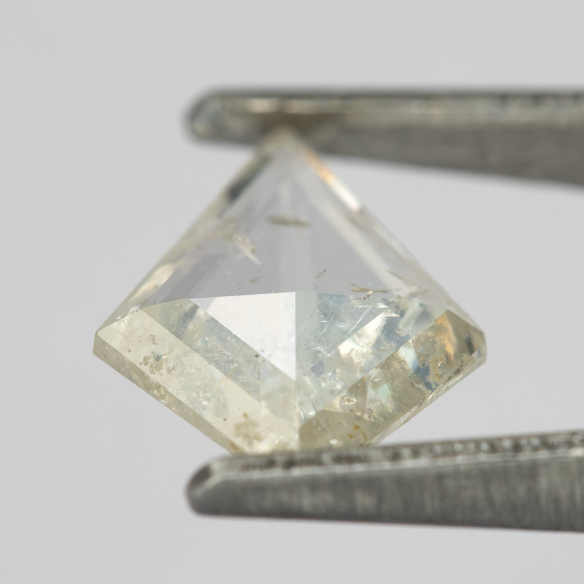 Tilted kite diamond in tweezers, showing crown facets, thickness and reflections.