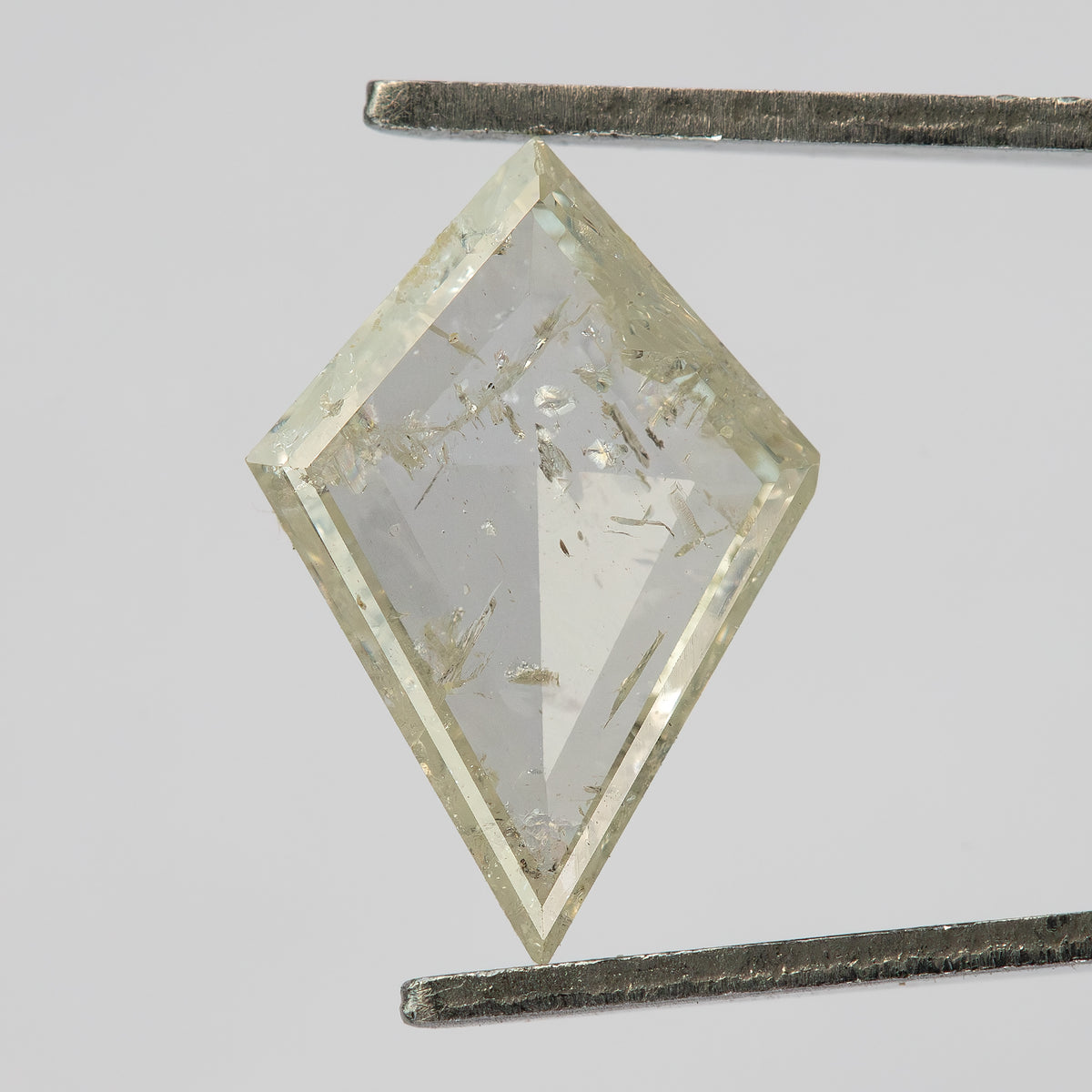 Reverse view of the kite diamond in tweezers, with a flatter central area and visible inclusions.