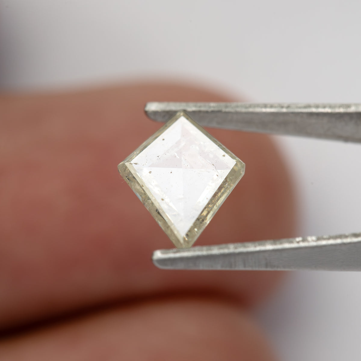 Tilted kite diamond reflecting pale light while held in tweezers.