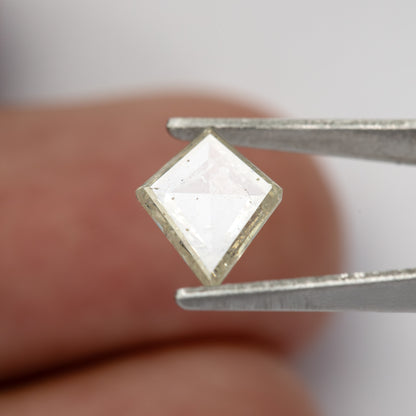 Tilted kite diamond reflecting pale light while held in tweezers.