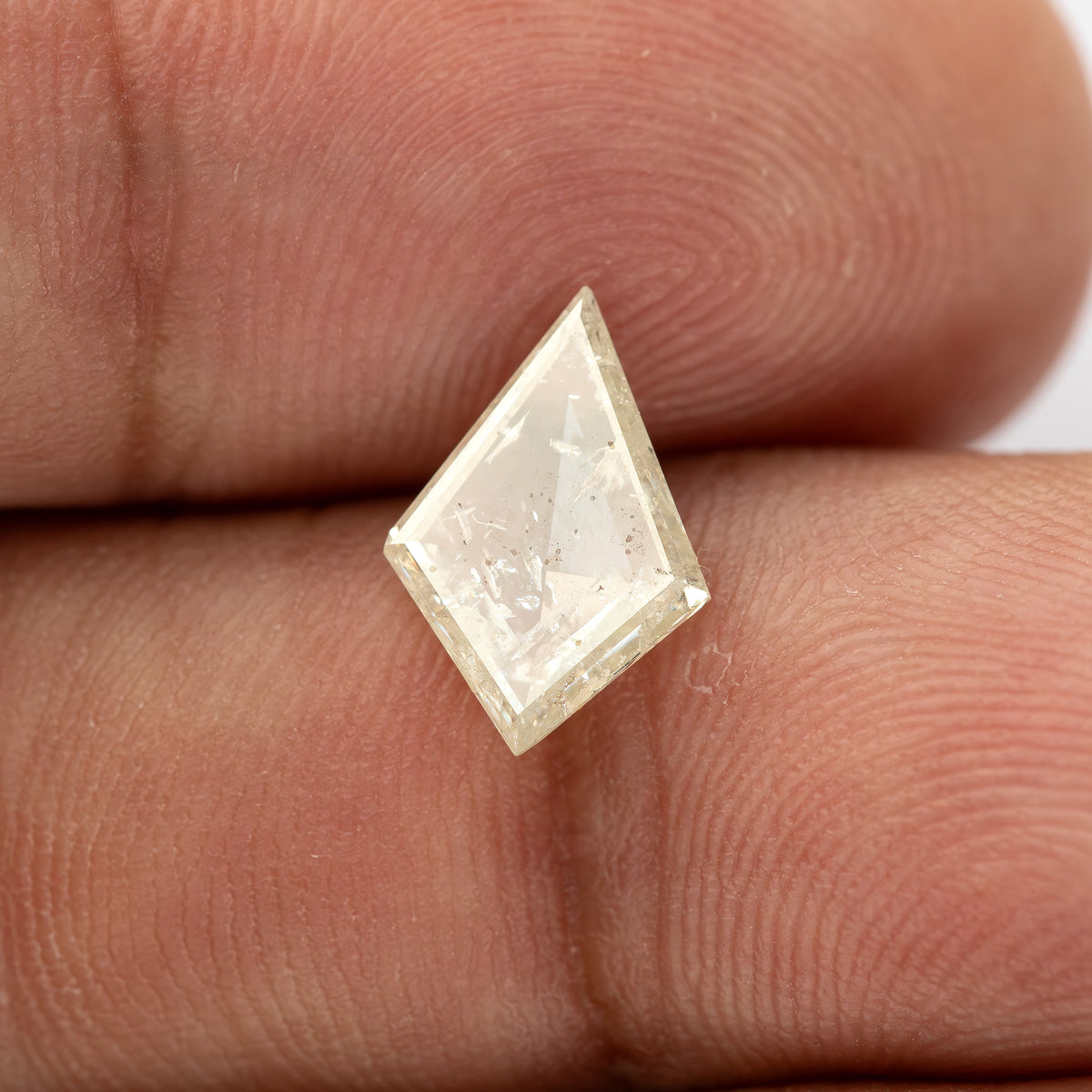 Pale kite diamond resting on a fingertip, showing its size against skin ridges.