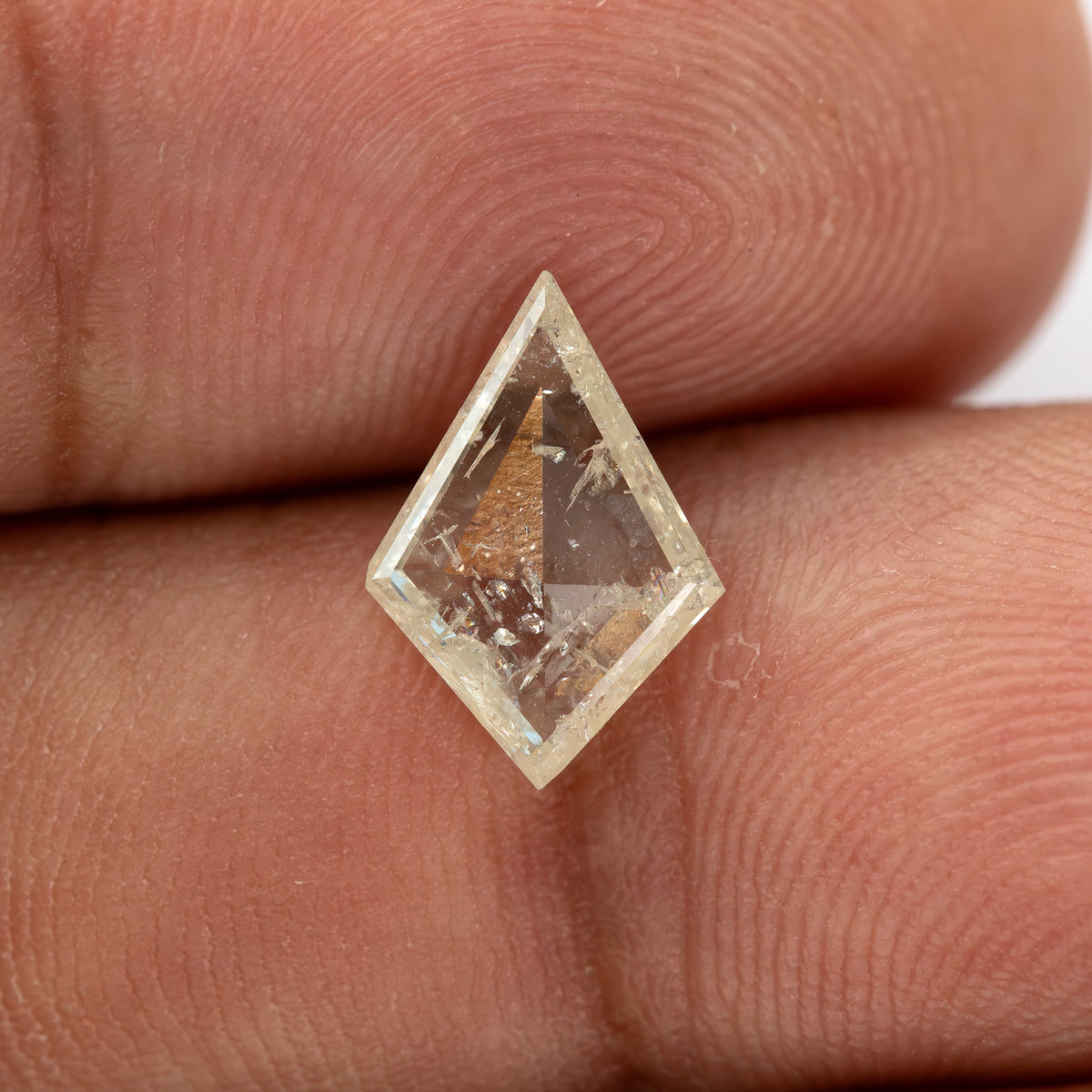 Kite diamond on a fingertip with internal inclusions visible against the warm skin background.