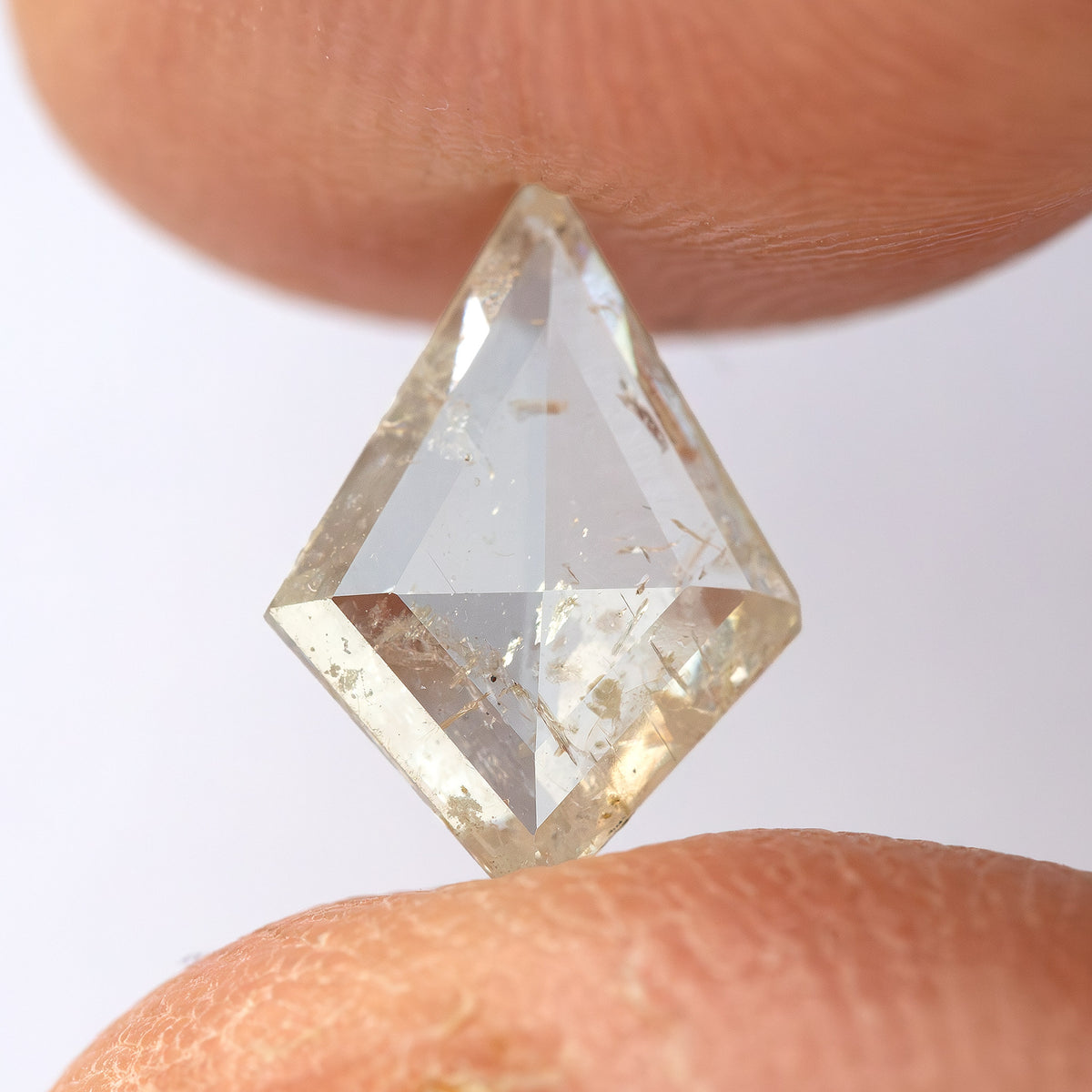 Face-up kite diamond between fingertips, showing the angular crown facets.