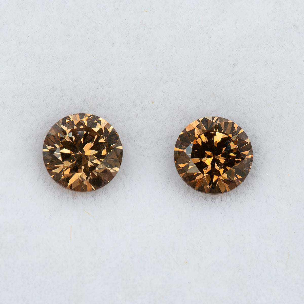 Two round cognac-brown diamonds side by side on white padding, shown close-up with amber-gold facet reflections and darker centers.