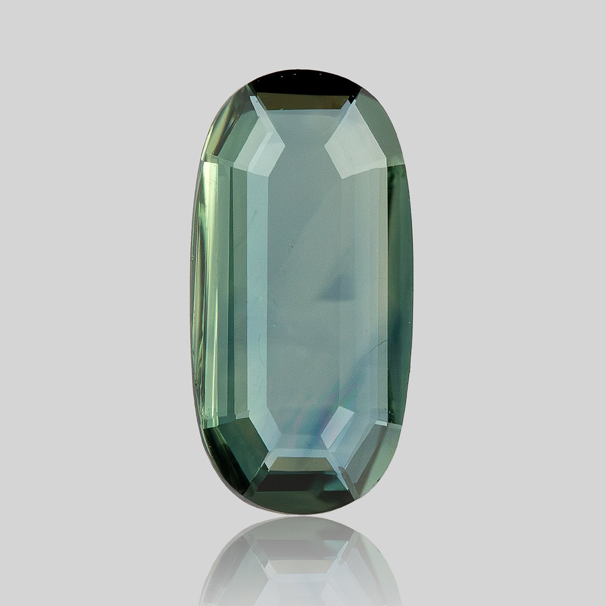 Broad-face view of the green-blue oval sapphire, with a transparent center, stepped border and reflection beneath.