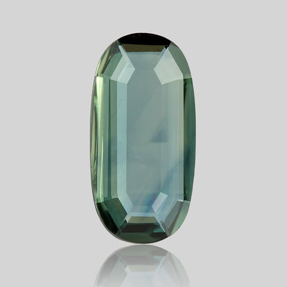 Broad-face view of the green-blue oval sapphire, with a transparent center, stepped border and reflection beneath.
