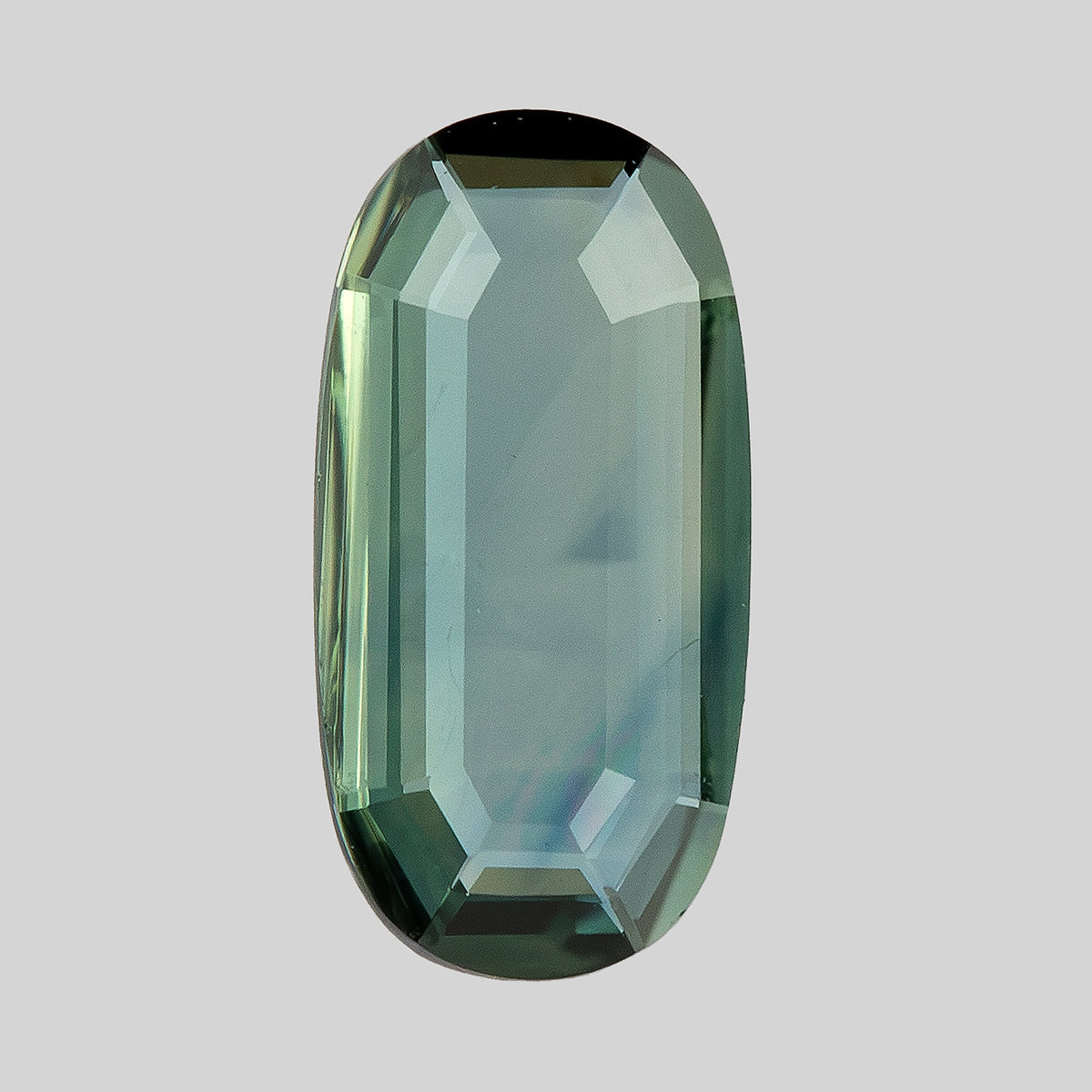 Slightly angled broad-face view of the green-blue portrait-cut oval sapphire against a light background.