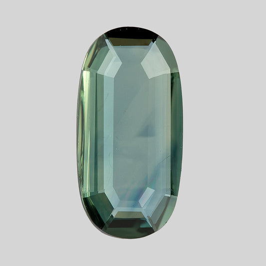 Slightly angled broad-face view of the green-blue portrait-cut oval sapphire against a light background.