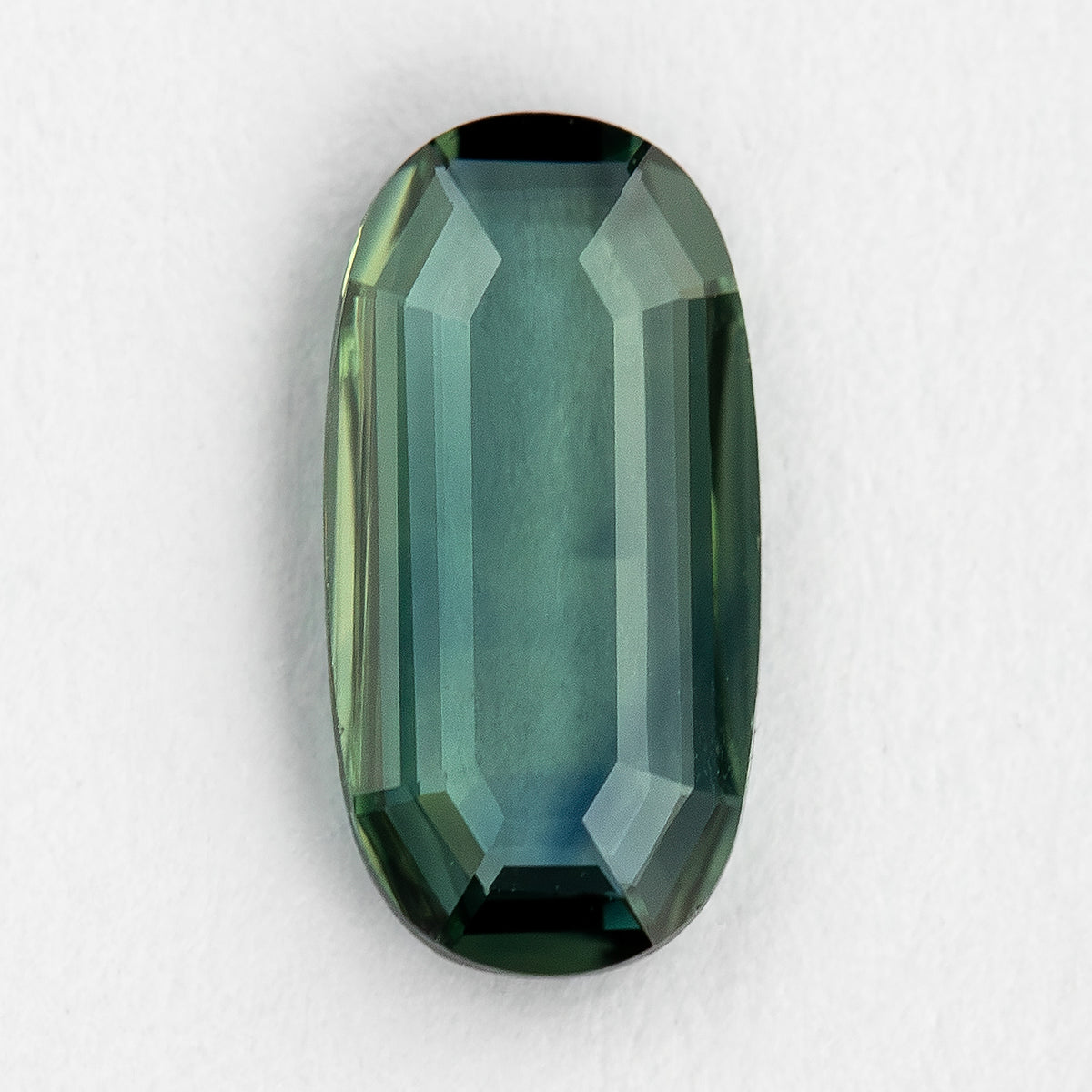 Green-blue oval sapphire on a white textured surface, showing the transparent center and dark stepped rim.
