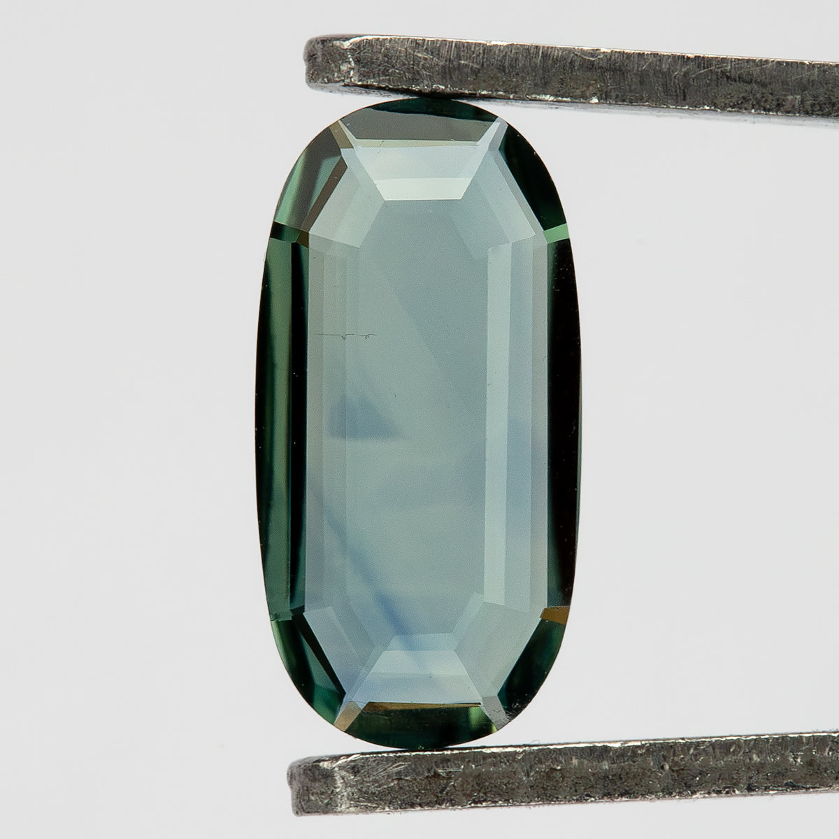 Angled tweezers view of the green-blue oval, with narrow reflective border facets and a broad transparent face.