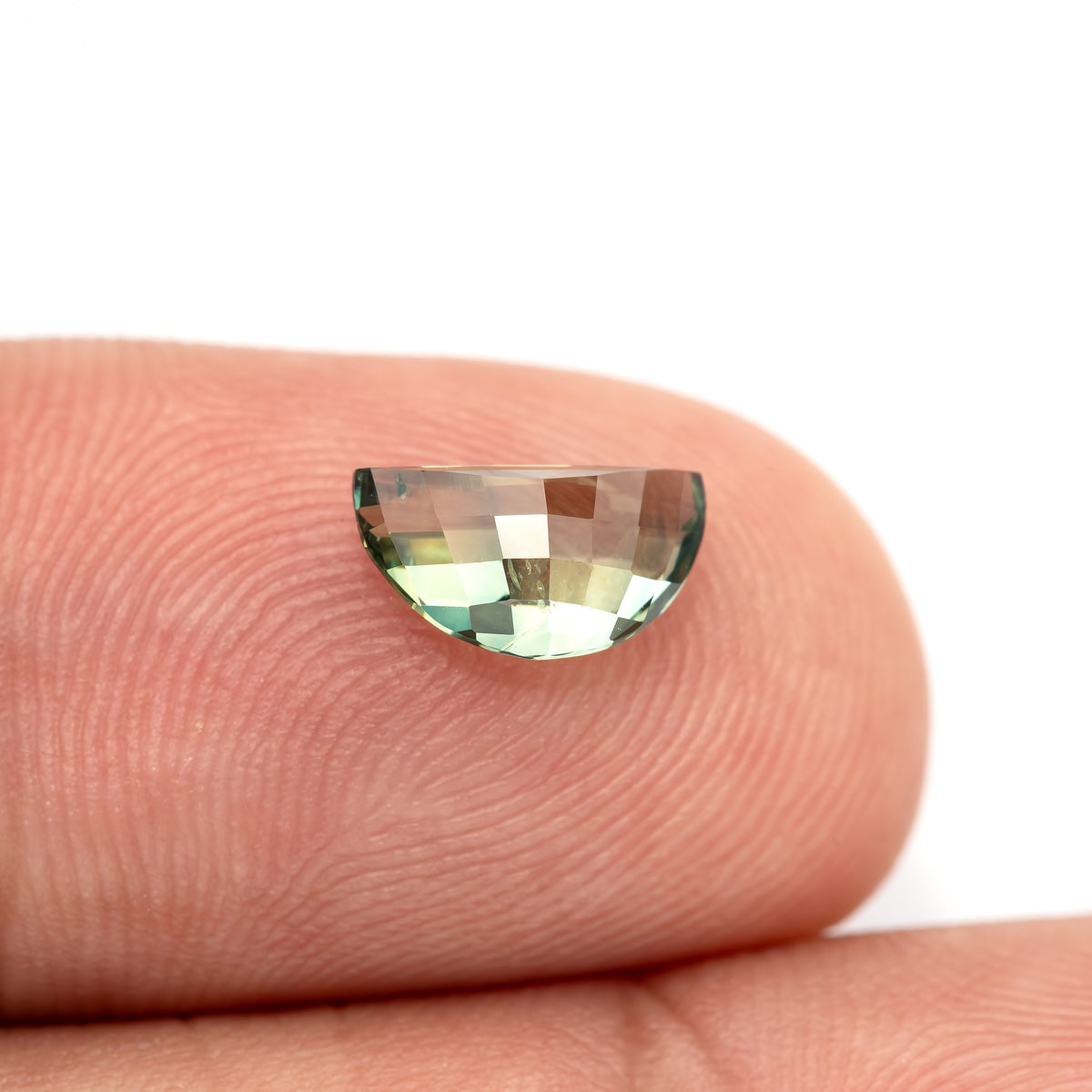Checkerboard pavilion of the half-moon sapphire resting on a fingertip, with light yellow-green and darker green reflections.