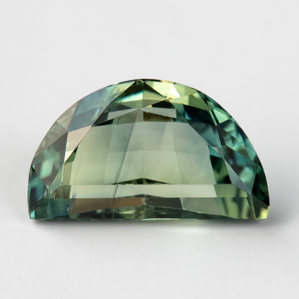 Face-up half-moon parti sapphire on a white background, with teal-blue-green reflections around the curved rim and a lighter yellow-green centre.