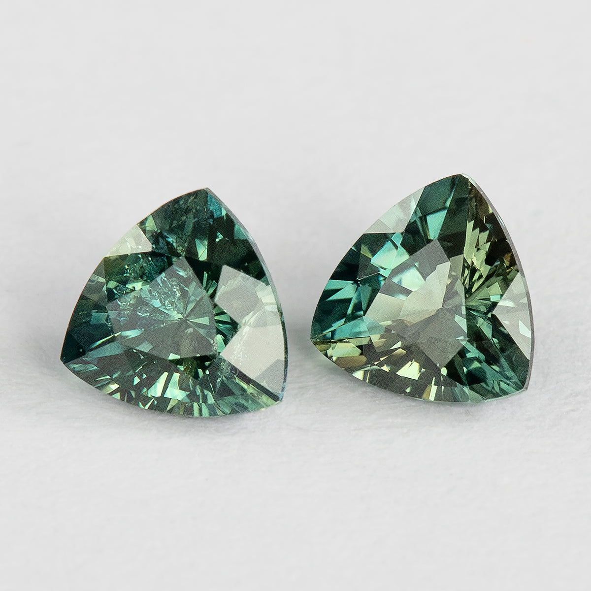 The sapphire pair at a tilted face-up angle, showing blue-green and yellow-green reflections across the facets.