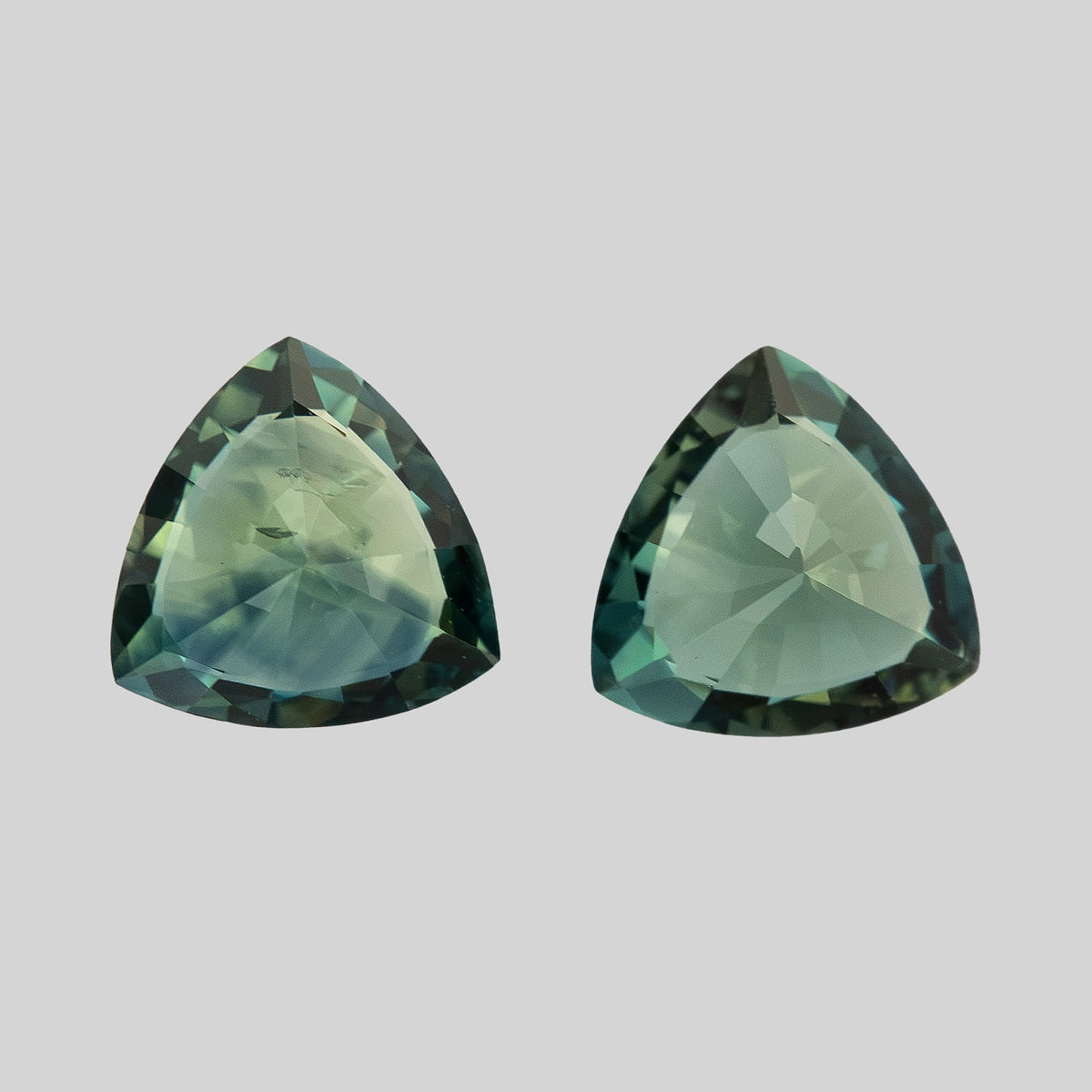 Close-up angle of both sapphires with broad pale reflections and visible internal characteristics in one stone.