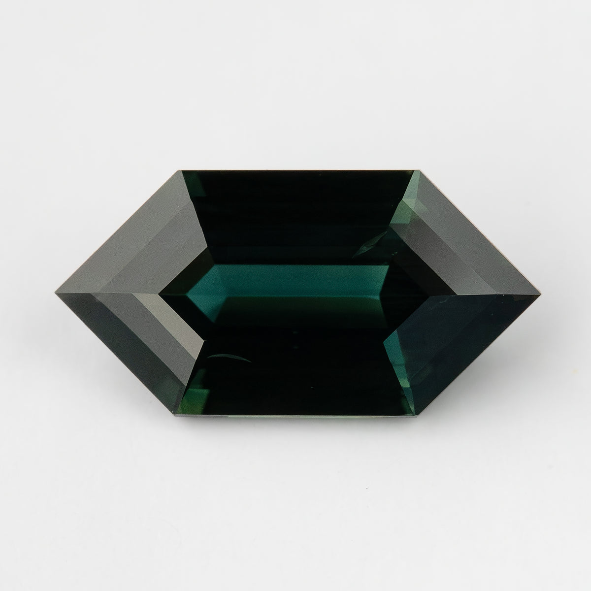 Horizontal face-up view of the elongated sapphire on a pale background, showing its dark teal appearance at this angle.