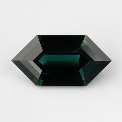 Horizontal face-up view of the elongated sapphire on a pale background, showing its dark teal appearance at this angle.