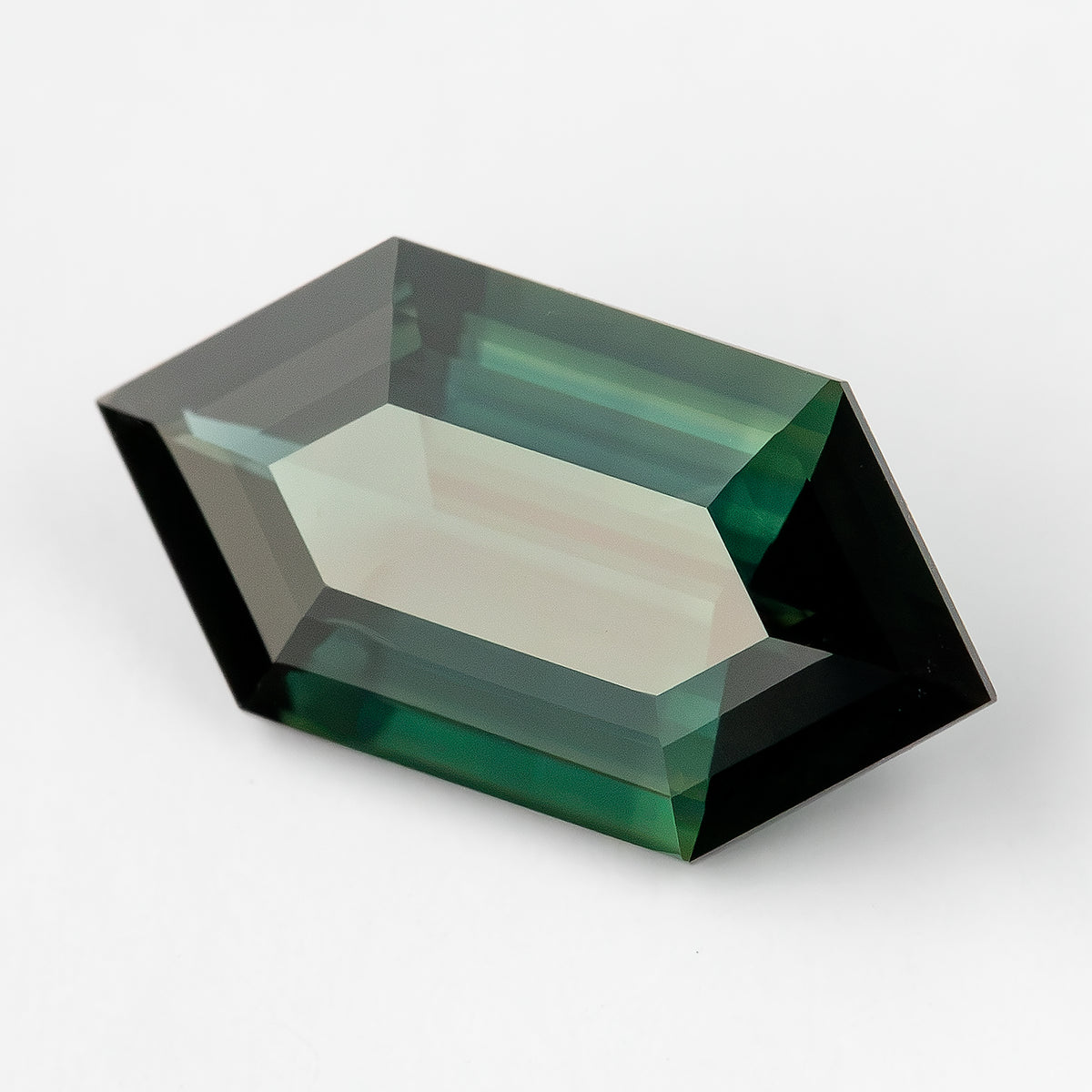 Angled crown-side view of the green-blue sapphire on a pale surface, showing its broad table, step facets and pale central reflection.