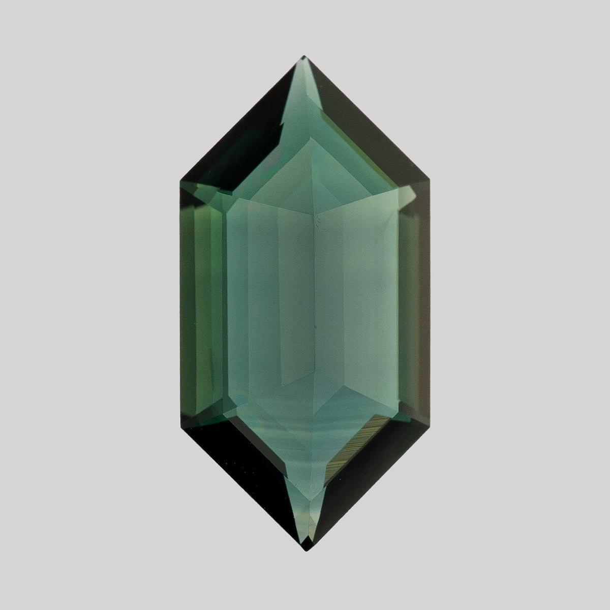 Upright reverse-side view of the elongated sapphire, with green-blue reflections, stepped facets and pointed ends.