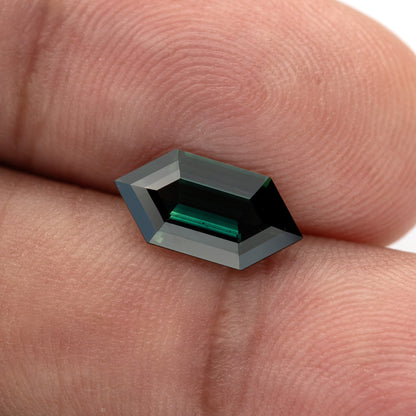 Angled between-fingers view of the sapphire, with a dark centre, bright green step reflections and small visible features.