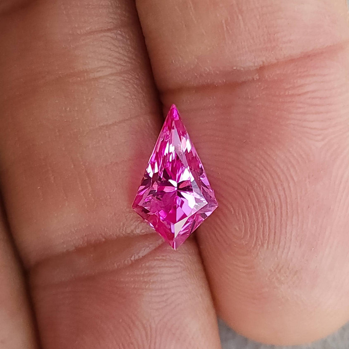 Vivid pink geometric kite cut faceted stone shown face-up on fingers for scale.